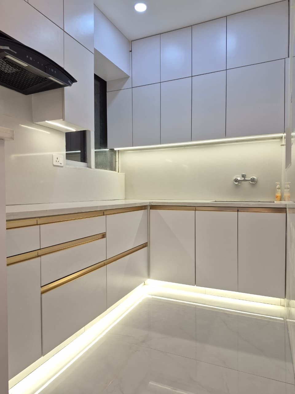 White modular kitchen with brass handle detail and under-cabinet lighting